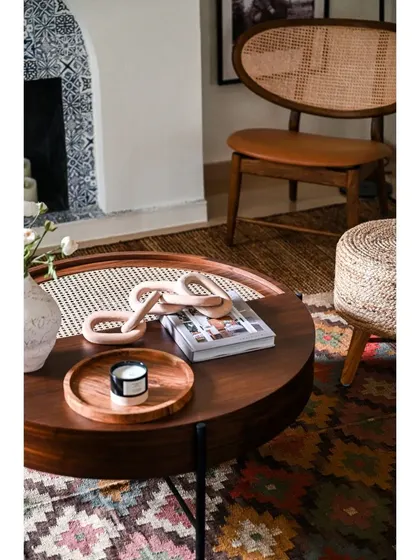 A close-up of the styling in the family room. The round coffee table with a caned insert, layered rugs, and a comfortable cane lounge chair all contribute to the warm, textured, and lived-in feel of this modern Spanish home.