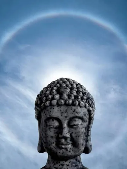 A stone Buddha statue is perfectly aligned with a natural sun halo, creating an image of peace and divinity. This is a unique and timely capture of a beautiful atmospheric phenomenon.