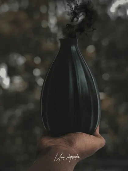A hand holds a black vase from which a plume of black smoke emerges, shaped like a dragon. This is a creative and moody conceptual image with a touch of fantasy.