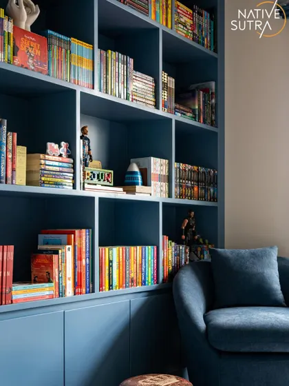 A stylish and functional room for a son, featuring a custom-built bookshelf in a striking deep blue. The grid-style compartments provide organized storage for books and collectibles, paired with a cozy reading armchair.