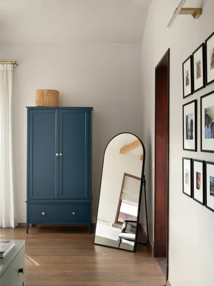 A classic blue armoire adds a pop of color and freestanding character to the primary bedroom. The gallery wall of family photos makes the space feel personal and loved.
