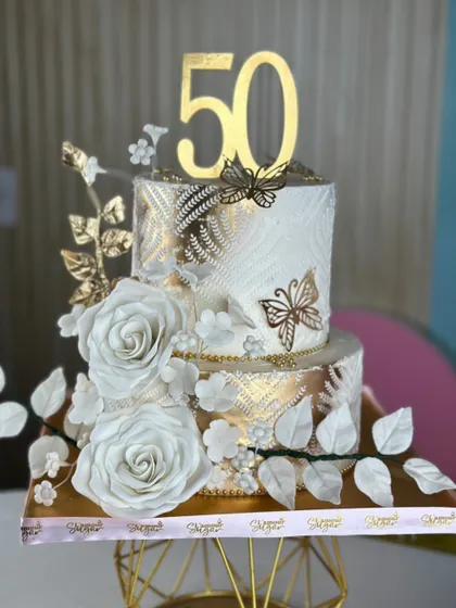 A symphony of white and gold to celebrate a beautiful love story. This elegant tiered cake features intricate textures, gold leaf details, and stunning handcrafted white sugar roses.