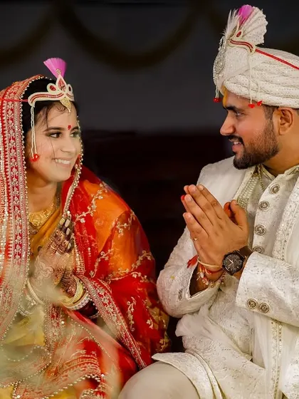The couple shares a sweet, smiling glance during their wedding ceremony. The groom's respectful 'namaste' gesture and the bride's happy expression capture a moment of mutual love and reverence.