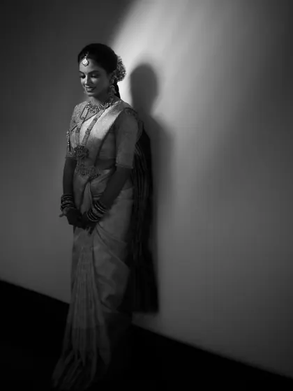 A simple and elegant black and white portrait. The bride stands against a plain wall, with the light creating a soft shadow, focusing all attention on her graceful presence.