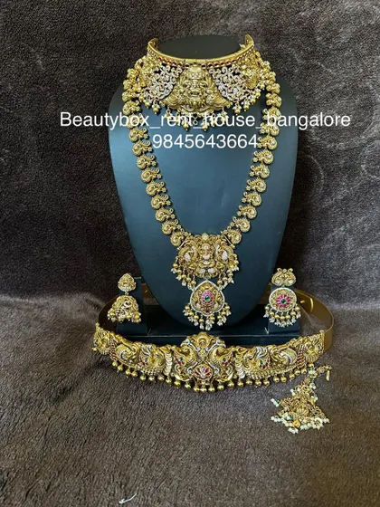 This rental set features a unique combination of a temple choker and a kasu-style long necklace, paired with a peacock-motif vaddanam.