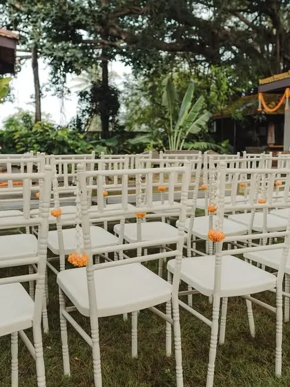 Simple white chairs for an outdoor ceremony, each adorned with a single marigold for a subtle pop of color.