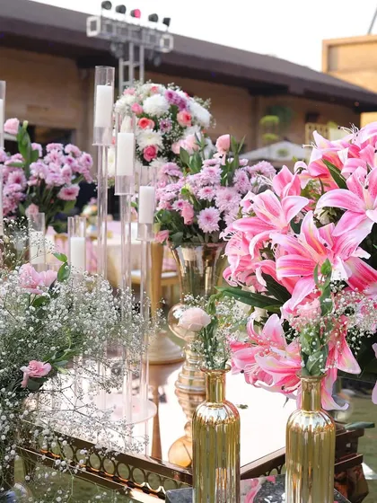 A stunning display of pink lilies and other flowers in golden vases. I use lavish floral arrangements like this to add color, fragrance, and a sense of luxury to the wedding decor.