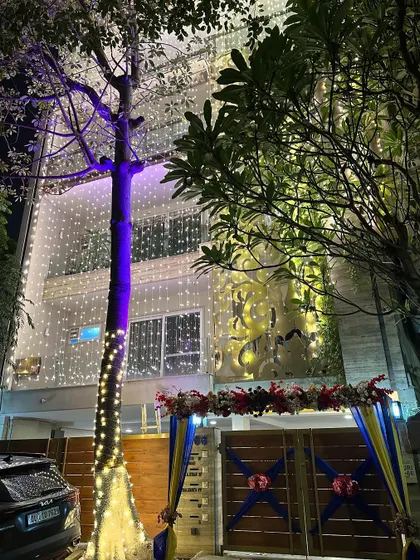 A full view of a wedding house at night. The entire building is lit up with fairy lights, and the entrance gate is decorated with colorful drapes and flowers.