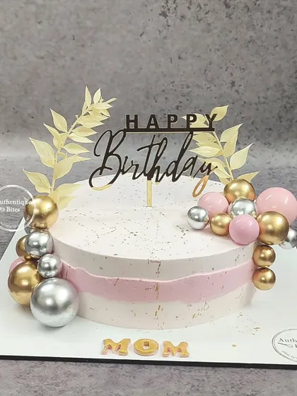 A classy strawberry cake with a simple, elegant design. The pink and white base is decorated with gold and silver spheres and delicate golden leaves.