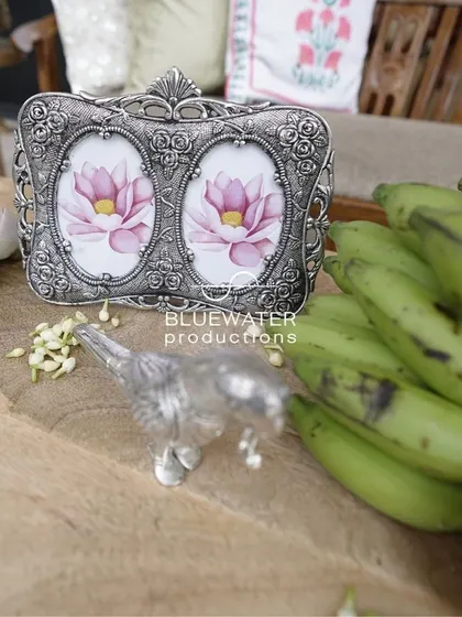 A silver photo frame with a lotus picture, placed next to fresh bananas, blending decor with tradition.