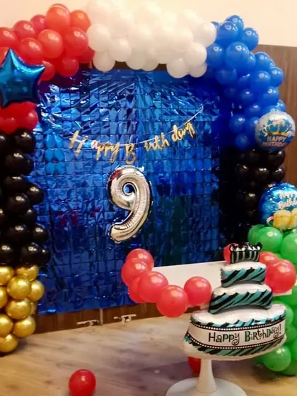 A simple yet effective home birthday setup for a 9th birthday. A blue foil curtain is framed by a balloon arch in primary colors.