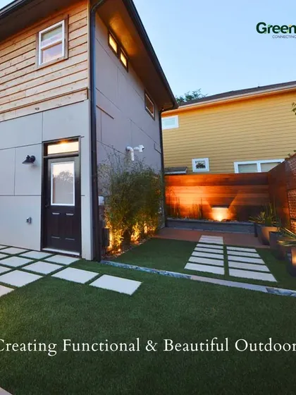 Creating functional and beautiful outdoors. This image shows a modern backyard with a combination of artificial turf and large stone pavers, complemented by subtle uplighting on the wooden fence.