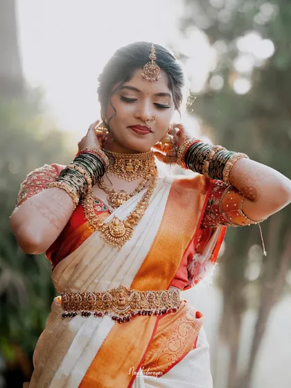 A portrait of the bride adjusting her necklace, highlighting the beautiful temple jewelry and her graceful hands.