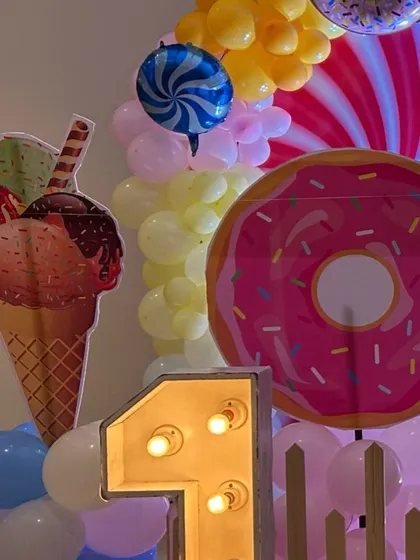 A sweet first birthday setup with a candyland theme, featuring a large light-up number "1" next to giant donut and ice cream props.
