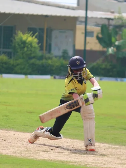 A young female player plays a confident front-foot drive, demonstrating excellent technique.