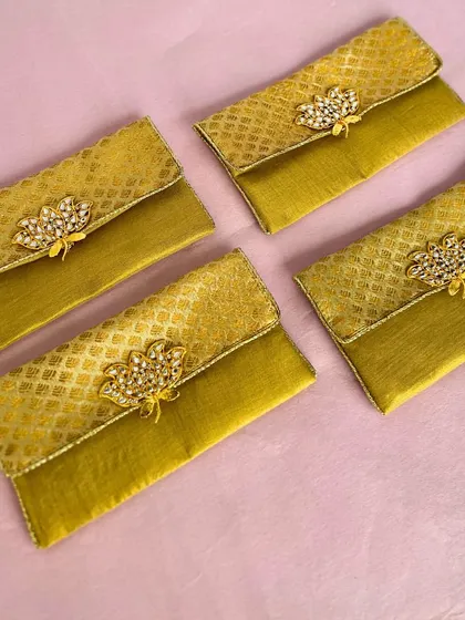 These elegant cash envelopes are made from a beautiful golden fabric and adorned with a kundan-style brooch. They are a luxurious way to present your shagun at a wedding.