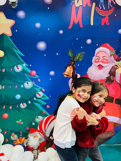Two happy girls with festive face paint, hugging in front of the Santa Claus backdrop during our Christmas party.