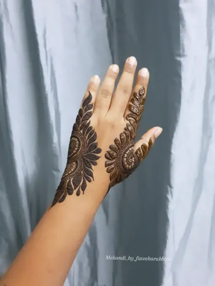 The completed bold henna design, featuring a large, leafy pattern that extends up the side of the hand.