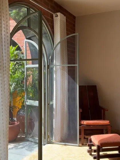 A detail of one of the arched doors, showing its connection to a cozy reading corner. The simple wooden chair and footstool create an inviting spot to enjoy the view and fresh air.