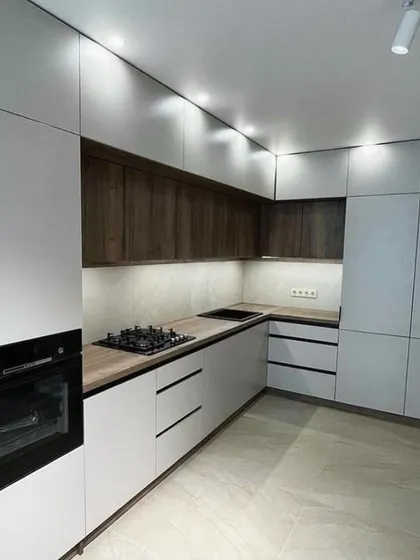 This perspective highlights the integrated tall unit and the dual hob setup (gas and induction). The layout is designed for a practical and efficient cooking experience.