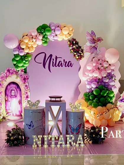 An enchanting fairy-themed birthday party in shades of purple and green. The decor includes a magical door prop, butterfly accents, and a custom name sign.