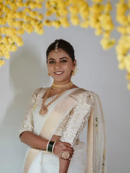 A smiling bride in a traditional Kerala saree, framed by an arch of yellow flowers.