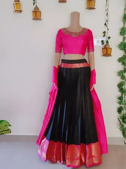 This black and pink lehenga is made from a traditional silk fabric with a gold border. The bright pink blouse features intricate handwork around the neckline.