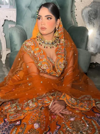 This full-length view shows the grandeur of the heavily embroidered orange lehenga. The makeup, though subtle in its color palette, is strong enough to balance the magnificent outfit.