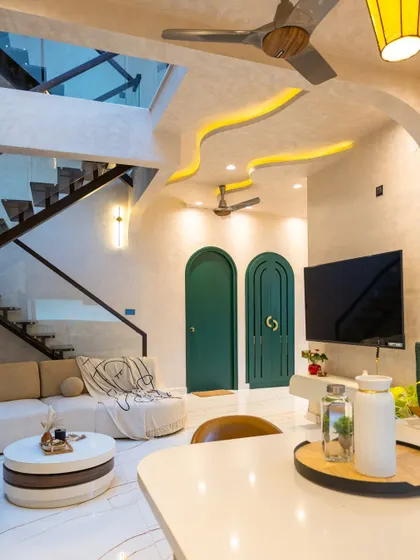 A view from the kitchen island into the living area, showcasing the open-plan layout, wavy ceiling with cove lighting, and bold green arched doors.