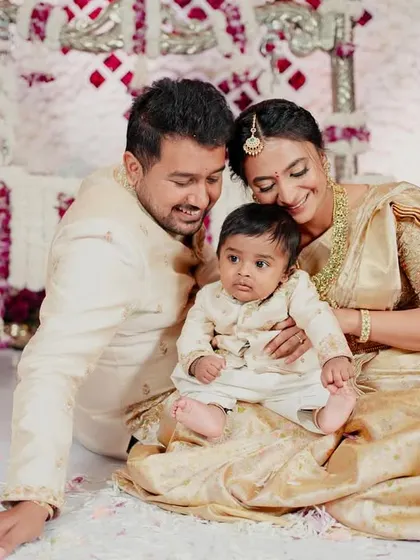 A sweet family moment on the floor amidst flower petals. Their matching cream and gold ensembles, from the saree to the sherwani and the baby's kurta, were all custom-made in our studio.