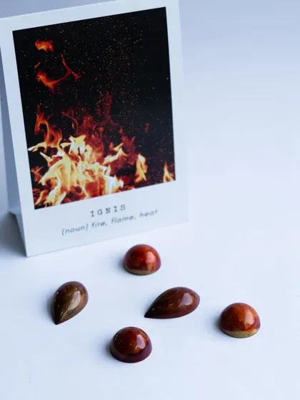 'Ignis', meaning fire. The design on these bonbons mimics the flickering flames and glowing embers of a fire, created with intricate cocoa butter coloring methods.