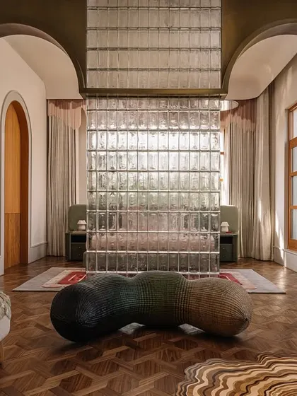 The guest bedroom in Rehethaan, where a glass block wall separates the sleeping area, creating a sense of privacy while allowing light to filter through. The room is a mix of textures, from the wooden parquet floor to the plush rugs.