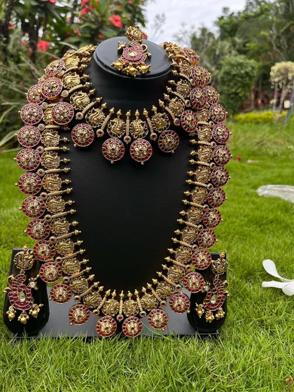An antique-finish coin necklace set with red stones. This rental includes a choker, a long haaram, and matching earrings.