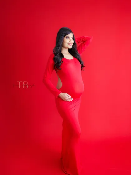 A bold and vibrant portrait. The mom-to-be stands against a solid red background, her matching red dress creating a powerful and modern look.