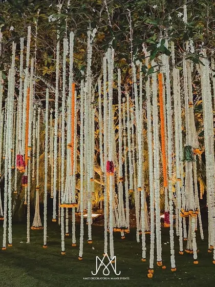 A beautiful installation of hanging floral strings (mogra and roses) from a tree, creating a fragrant and visually stunning canopy for an outdoor event.