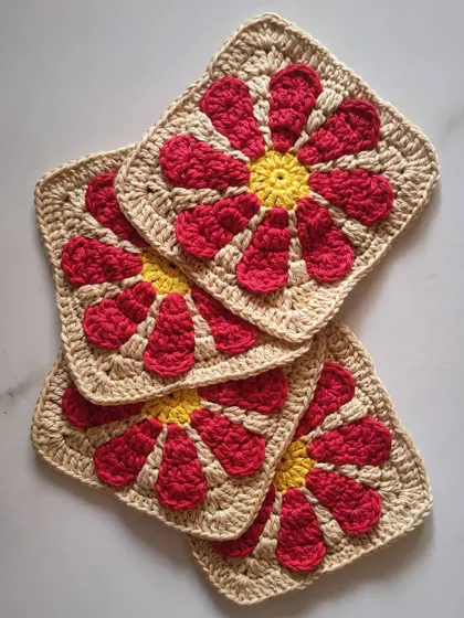 These are the individual granny squares that form the foundation of my Groovy Daisy bag. Each square is carefully stitched with a bright yellow center and red petals, ready to be joined into a beautiful and functional accessory.