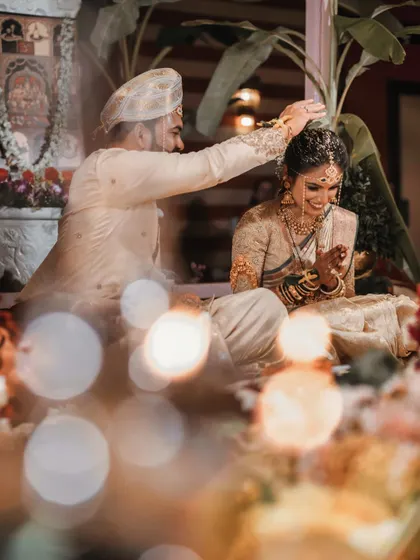 A beautiful moment of blessing, captured through a soft, warm bokeh of lights. The focus is on the couple's interaction during the ceremony, creating a dreamy and romantic feel.