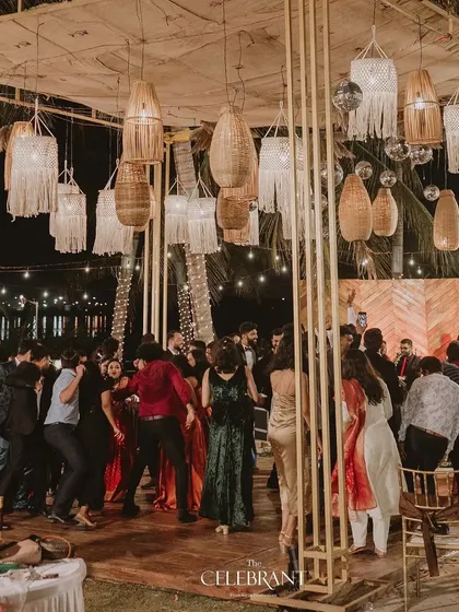 A rustic-themed party in full swing. Guests dance under a canopy of assorted wicker and macrame lamps, which provided warm, ambient lighting for this beachside reception.