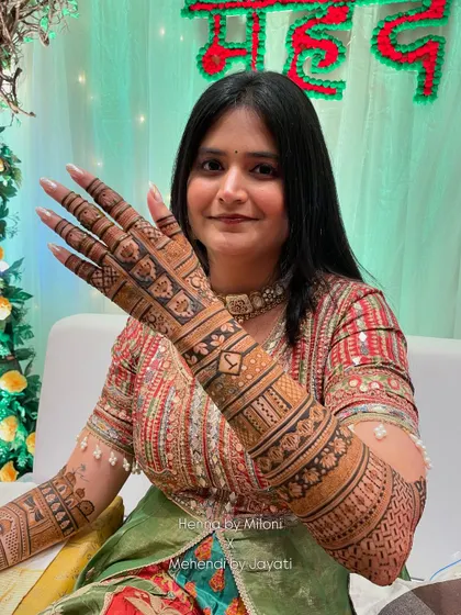 A close-up of the bride's beautiful smile and her intricate mehendi. The design on the back of her hand features geometric patterns and a central motif.