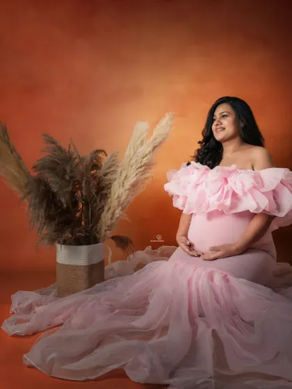 This mom-to-be looks serene and beautiful, cradling her bump in a delicate pink gown. The pampas grass adds a gentle, bohemian touch to the studio setup.