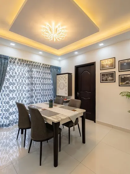 The dining area is elegant and simple, with a white marble-top table, grey upholstered chairs, and a beautiful ceiling light fixture.