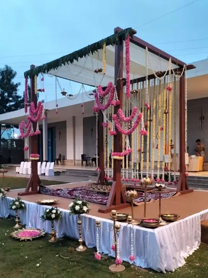 For this outdoor wedding, we designed a rustic yet elegant mandap with a wooden frame, draped in white fabric and adorned with beautiful pink and white floral garlands for a soft, romantic feel.