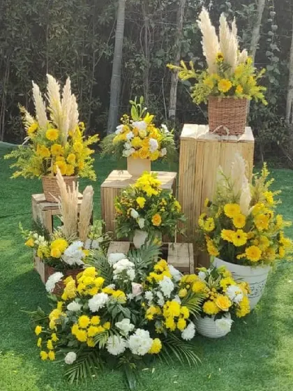A beautiful display of yellow and white flowers in rustic baskets and vases, arranged on wooden crates. This corner adds a touch of sunshine and natural charm to the event.