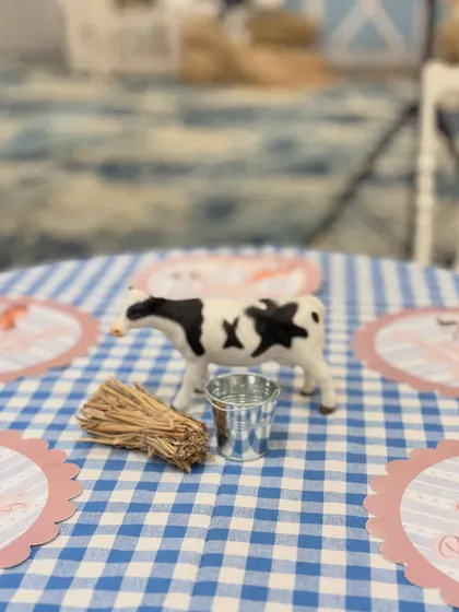 A close-up of the farm-themed centerpiece, with a toy cow, mini hay bale, and personalized placemat on a classic gingham tablecloth.