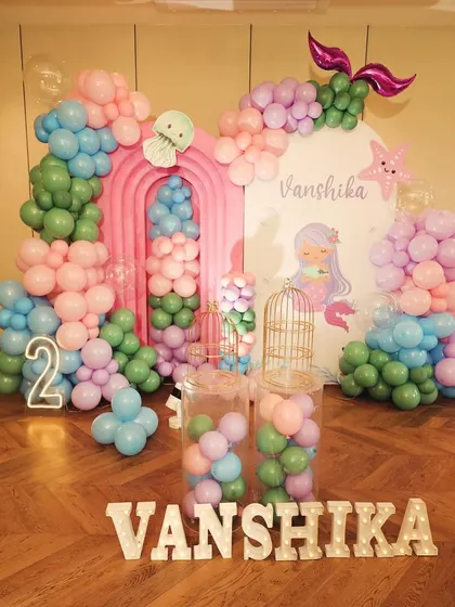 A full view of the mermaid party decor, including the light-up number '2', clear plinths filled with balloons, and a personalized backdrop.