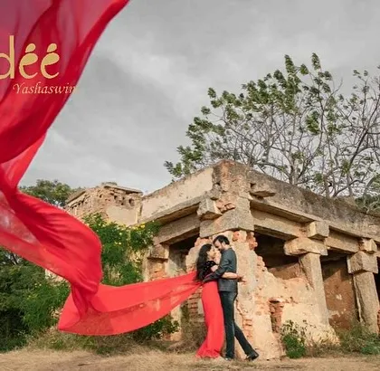 A dramatic pre-wedding shot featuring a vibrant red trail saree against ancient ruins. This shows how you can blend traditional wear with epic, cinematic photography.