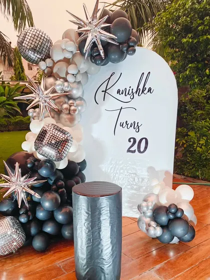 A sophisticated 20th birthday party in an outdoor setting. The decor features a black, white, and silver balloon arch with starburst and disco ball accents.