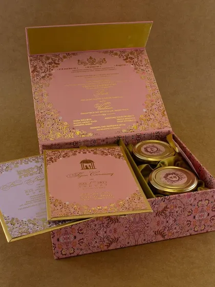A beautiful pink and gold patterned box that combines traditional motifs with a modern color palette. Inside, it holds the main card, multiple inserts, and two jars for gifts.