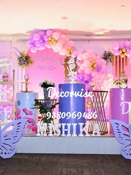 We create magical, fully-realized party themes like this enchanting butterfly wonderland for Mishika's first birthday. This grand stage setup features large butterfly wing cutouts, personalized marquee letters, a custom backdrop with a neon sign, and coordinated balloon garlands, all designed to create a perfect photo opportunity.
