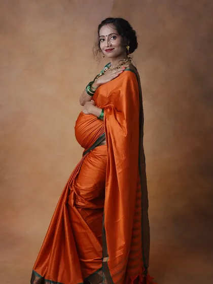 An elegant portrait of a mom-to-be in a vibrant orange silk saree. The simple, classic pose against a neutral background creates a timeless piece of art.
